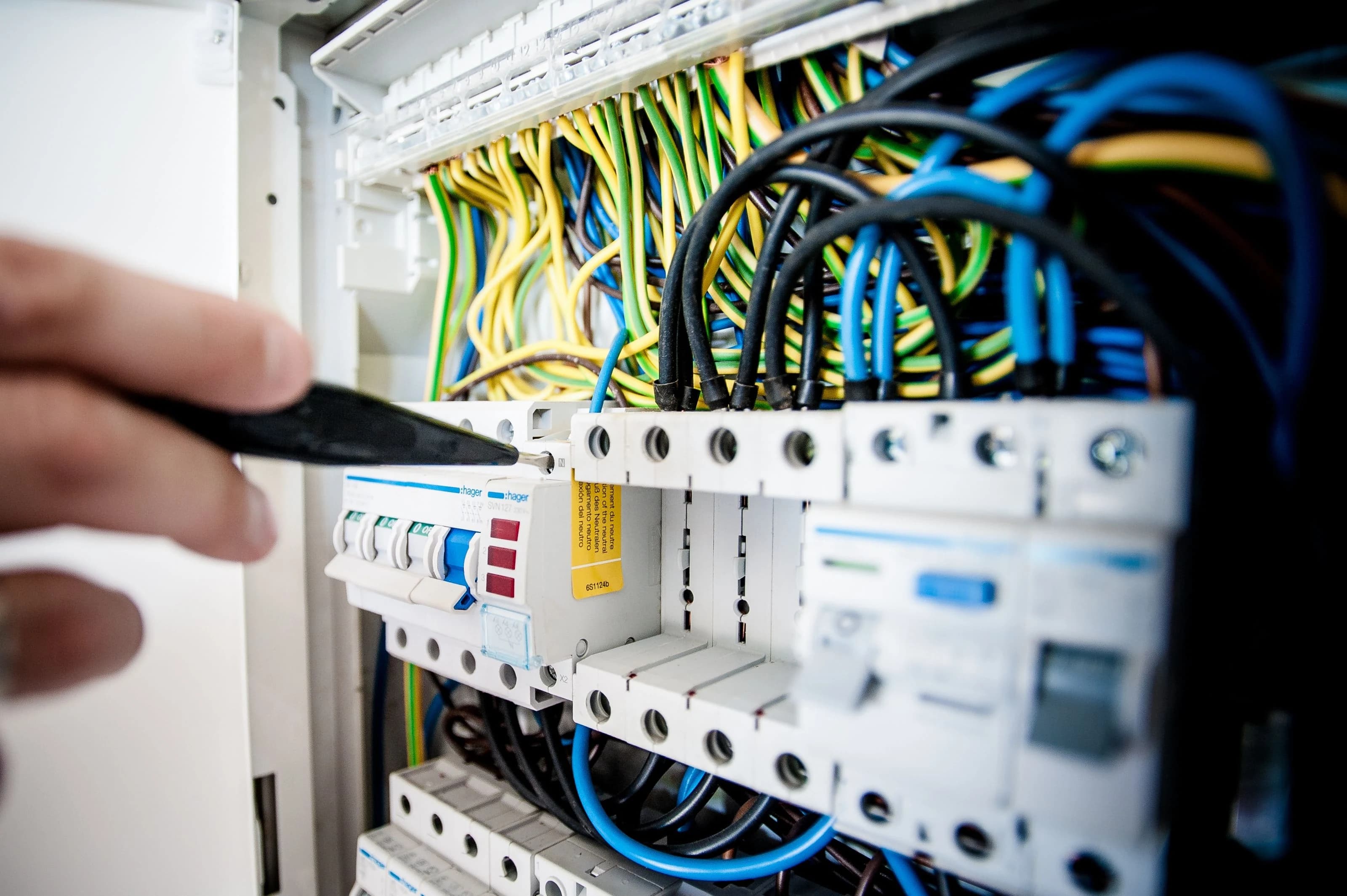 An electrician using a tool at a circuit breaker panel with neatly arranged wiring.