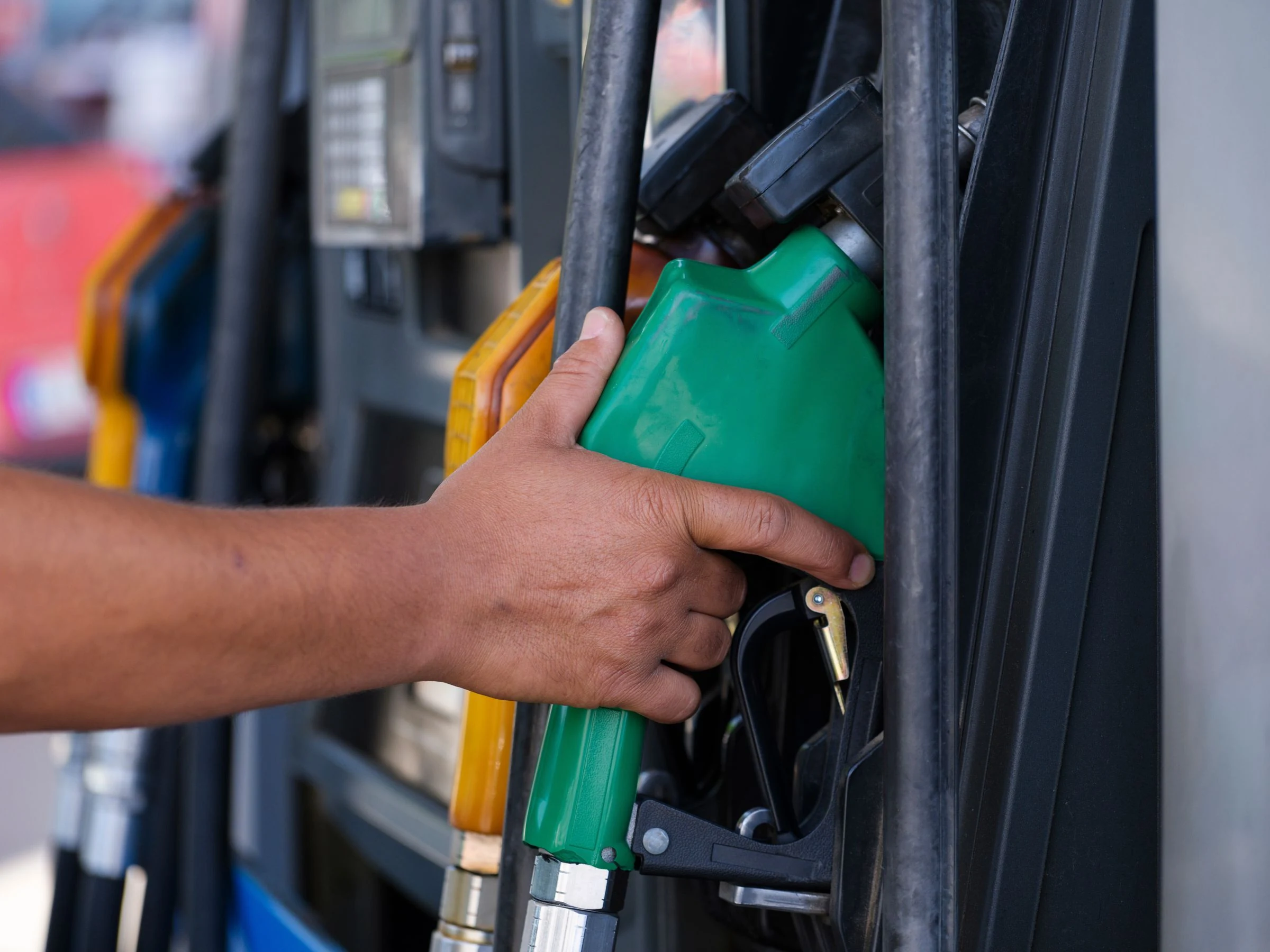 A hand holding a green fuel nozzle at a petrol pump.