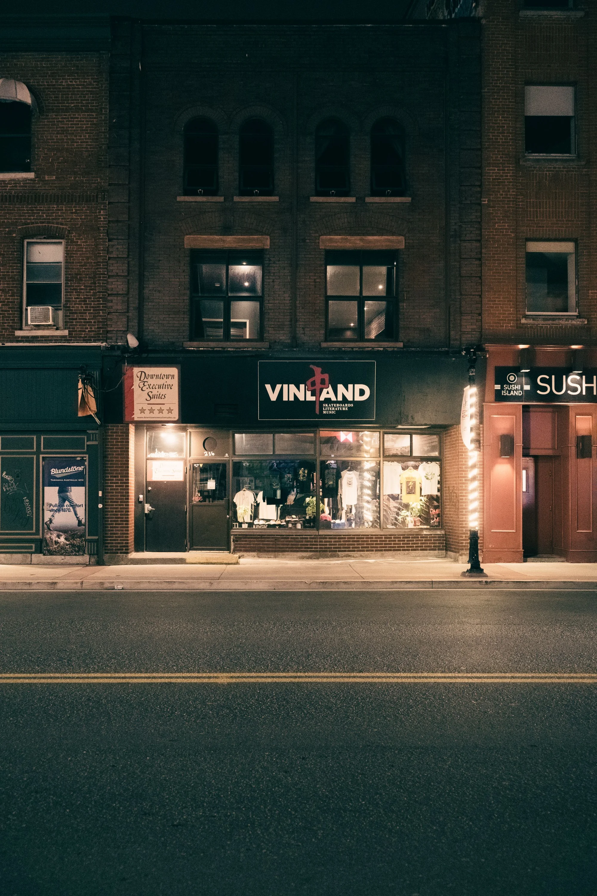 A warmly lit shop window on a quiet street at night, beneath a dark brick facade.